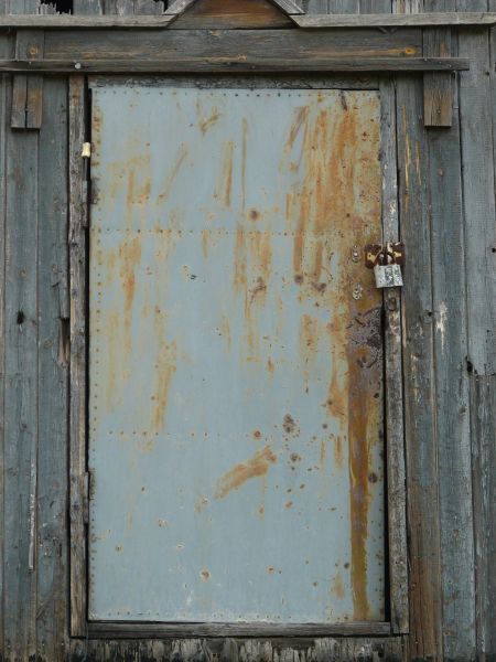 Rusting metal door in light blue shade with spots and streaks of rust.
